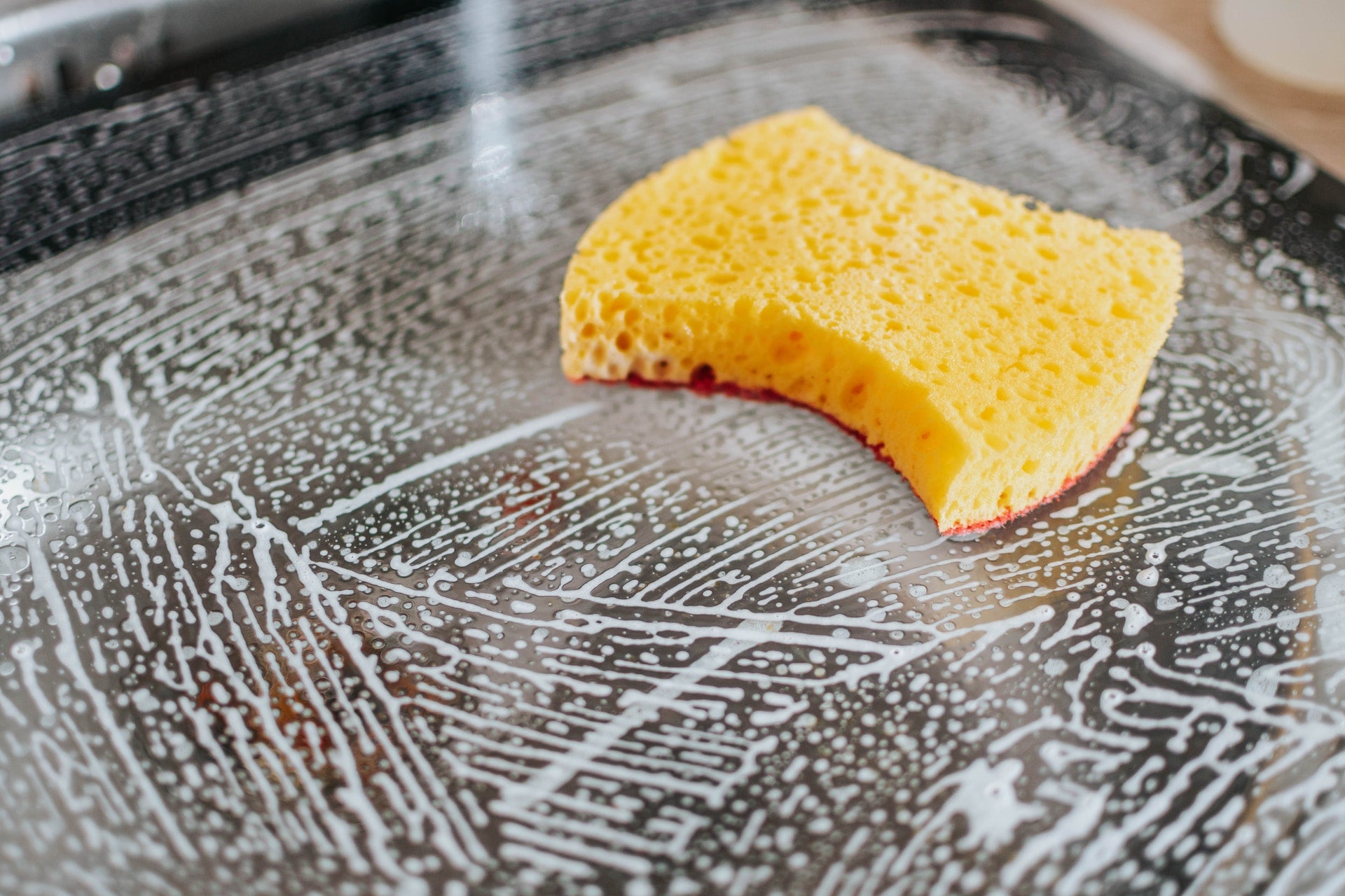 Yellow sponge on soap covered metal surface.
